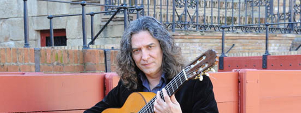Tomatito mirando a la cámara mientras sostiene la guitarra apoyado en la barrera de una plaza de toros